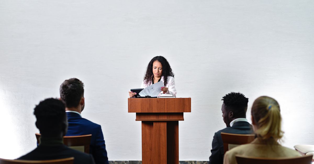 Confident woman delivering a speech to a diverse audience in a conference room.